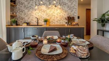 A dining area with a table set for a meal, featuring a placemat, plates, cutlery, and a glass container with pastries.