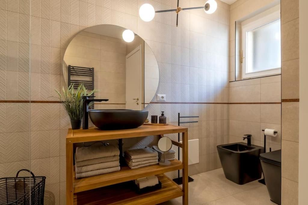 Un bagno moderno con un mobile bagno in legno, uno specchio grande, un lavandino nero e una finestra.