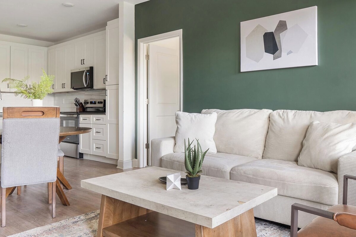 A modern living room with a sofa, coffee table, and a dining area with a chair and a plant.