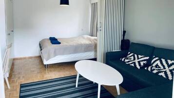 Una stanza compatta con un letto, una divisa, un tavolino e una lampada a sospensione.