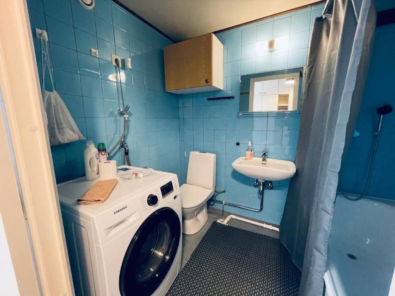 Baño compacto con lavadora, inodoro, lavamanos y ducha.