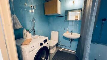 Baño compacto con lavadora, inodoro, lavamanos y ducha.
