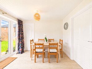 Un coin repas avec une table ronde et six chaises, un luminaire suspendu et une vue à travers une porte vitrée.