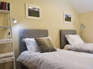 Ein Hotelzimmer mit zwei Betten, einem Bücherregal und zwei gerahmten Bildern an der Wand.