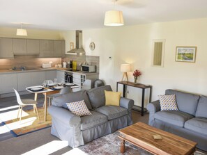Eine moderne Küche mit Mikrowelle, Toaster und Spüle. Zwei graue Sofas mit gemusterten Kissen, ein Holztisch und ein kleiner Beistelltisch mit Lampe.