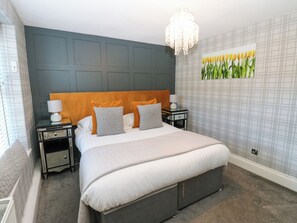 A bedroom with a bed, nightstands, a chandelier, and a wall painting. - Crown Cottage (Appleby-in-Westmorland)