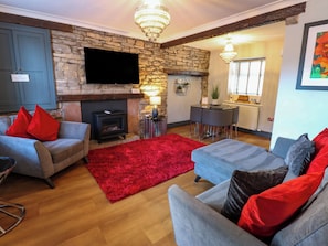 A living room with a stone fireplace, a flat-screen TV, and a dining area with a table and chairs. - Crown Cottage (Appleby-in-Westmorland)