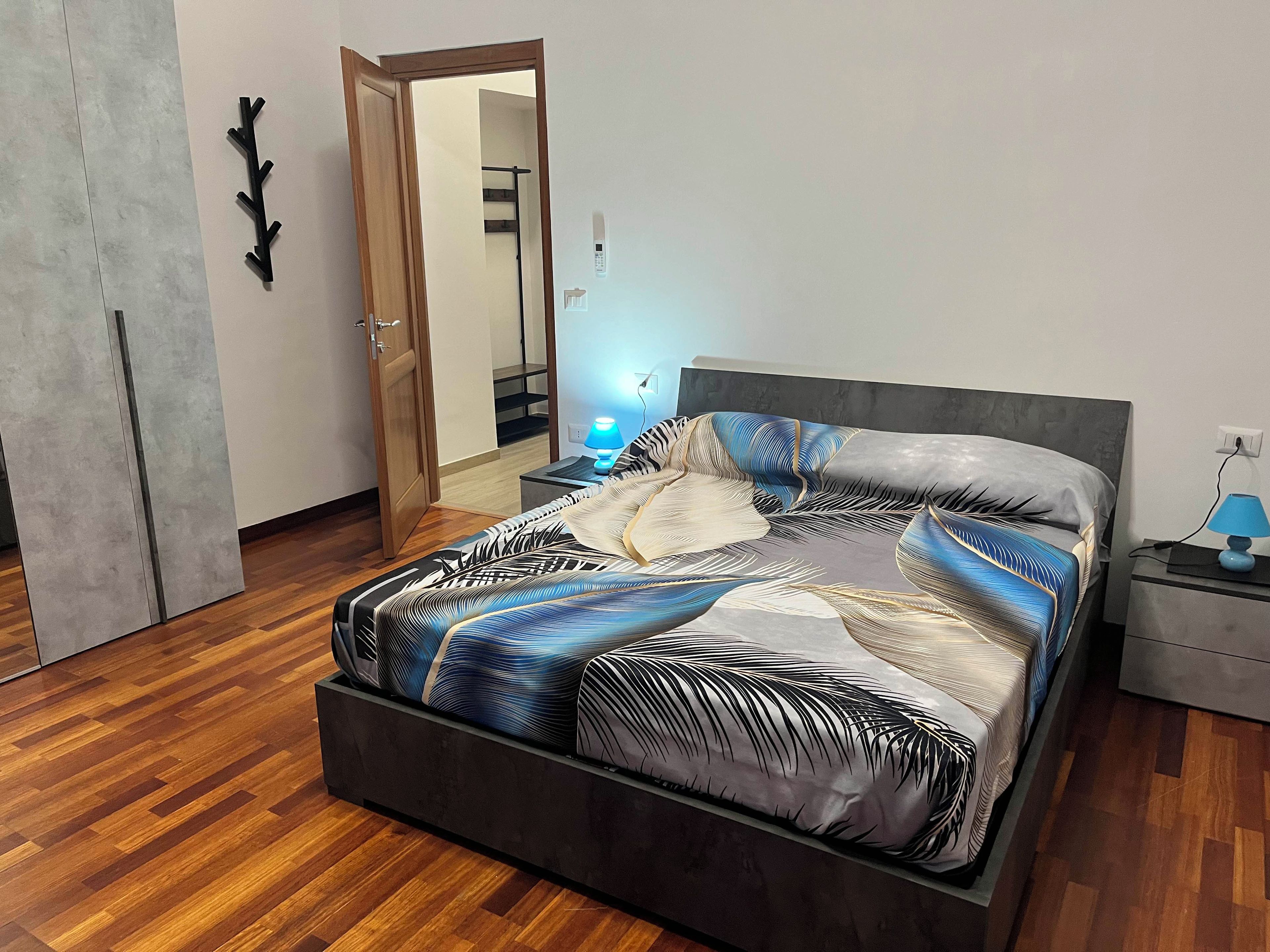 Ein modernes Schlafzimmer mit Bett, Nachttischen, einer Wandleuchte und einer Tür zu einer Treppe.