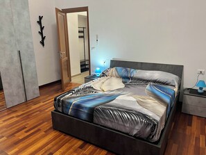 Une chambre moderne comprenant un lit, des tables de chevet, une commode, une lampe fixée au mur et une porte donnant sur un escalier.