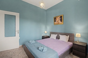 A bedroom with a bed, two bedside tables, a nightstand, a door, and a painting on the wall.