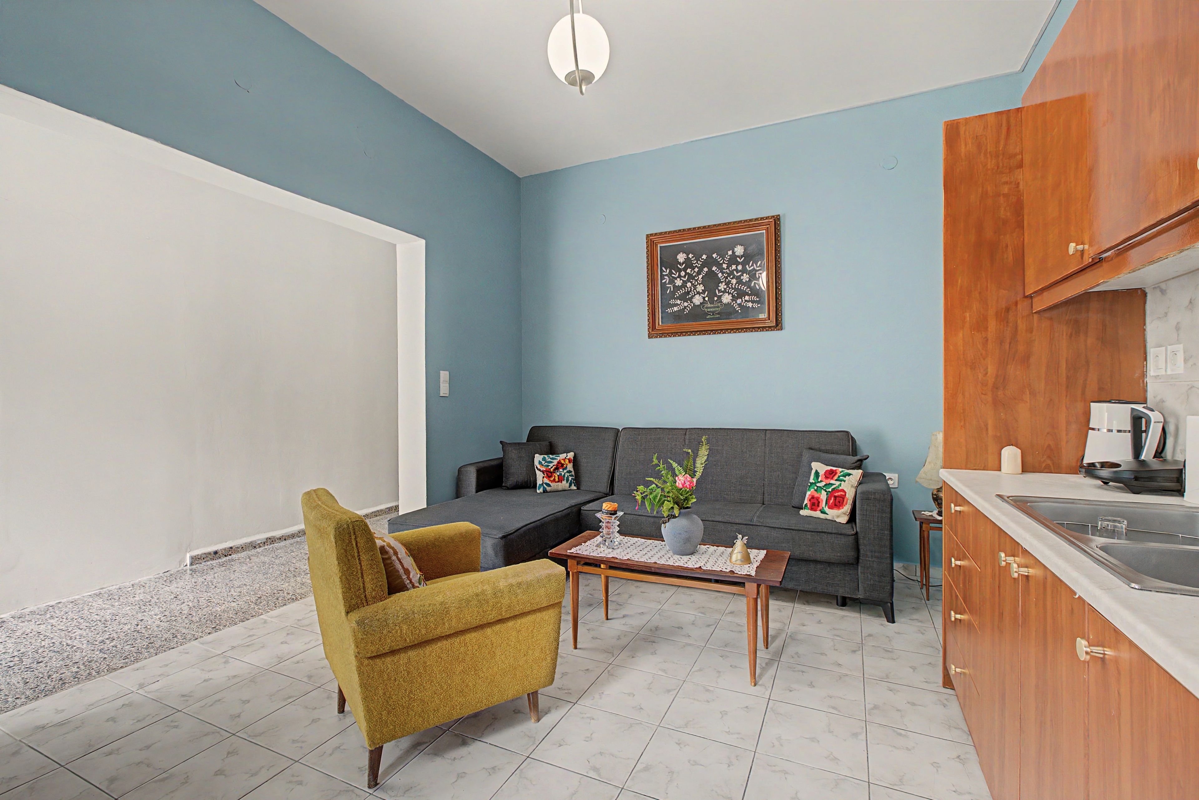 A compact living space with a sofa, armchair, coffee table, and a kitchen area with cabinets and a sink.