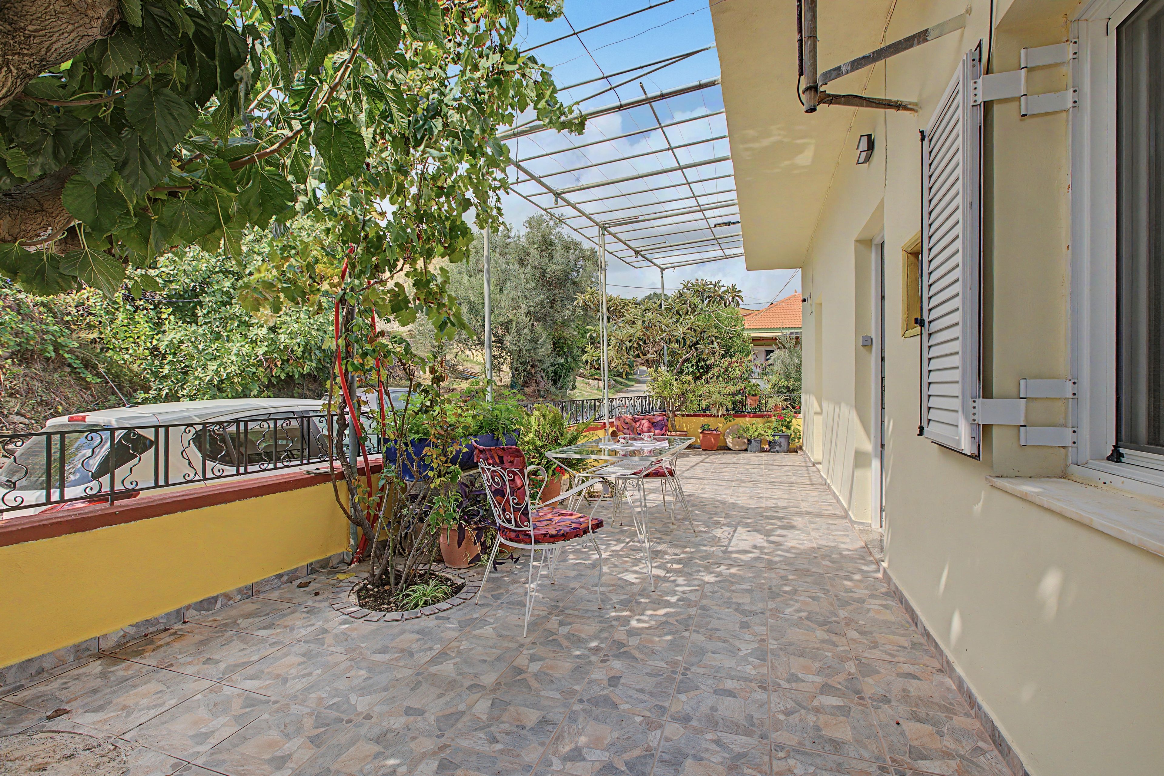 A covered outdoor patio with stone flooring, potted plants, and outdoor furniture.