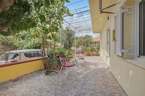 Une terrasse extérieure couverte, dotée d’un sol en pierre, de plantes en pot et de mobilier d’extérieur.