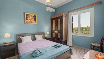 A bedroom with a bed, a nightstand, a lamp, a wardrobe, a window with a view, and a painting on the wall.