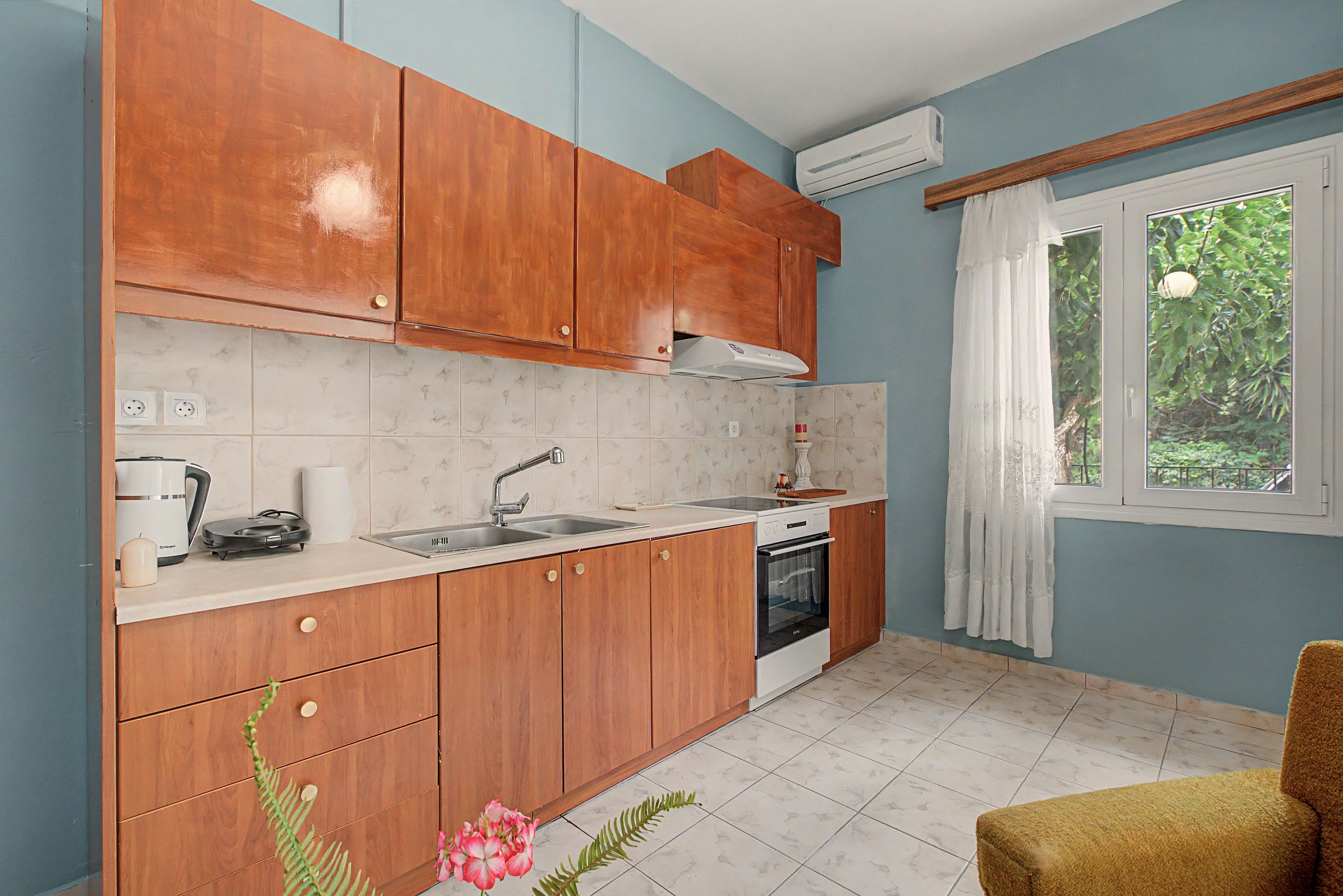 A compact kitchen with wooden cabinets, a built-in oven, a sink, and a window with a view of greenery.