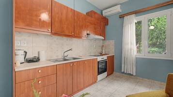 A compact kitchen with wooden cabinets, a built-in oven, a sink, and a window with a view of greenery.
