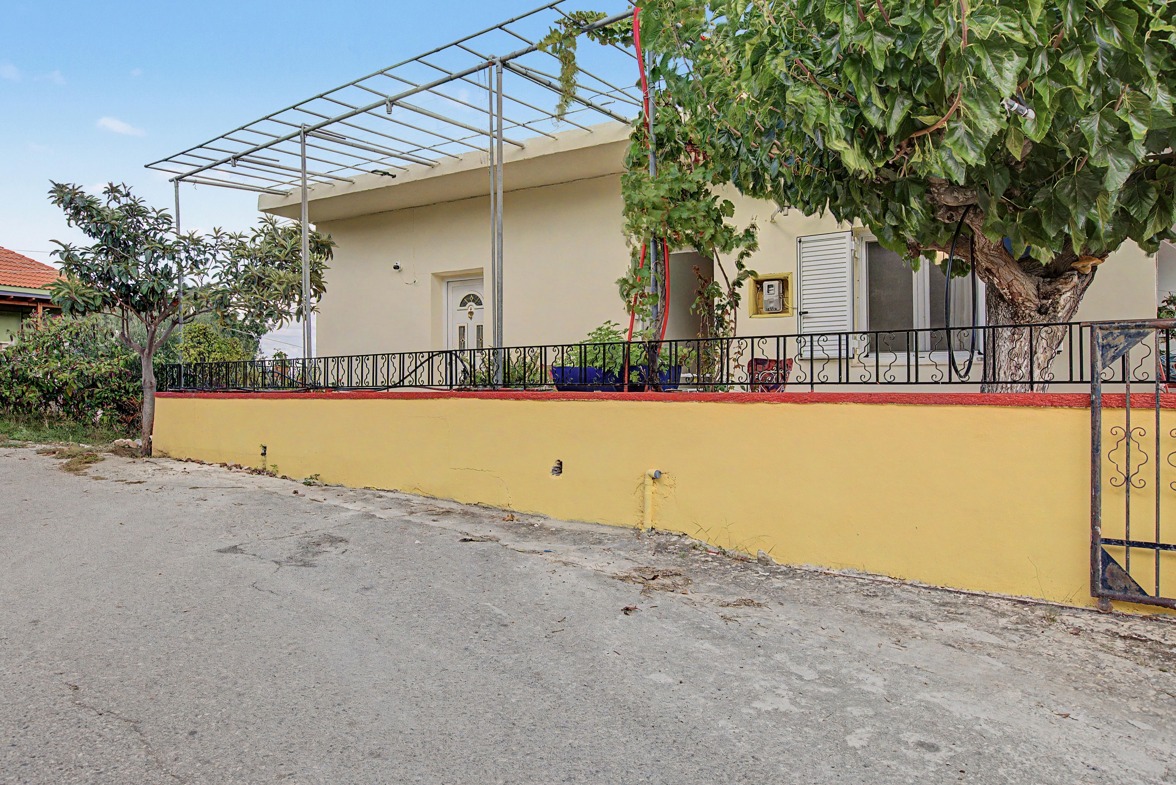 A building with a yellow wall, a metal fence, and a tree with green leaves.