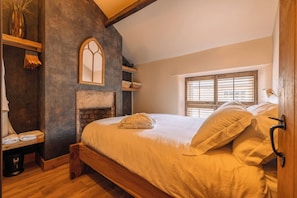 A bedroom with a wooden bed, a fireplace, a window with blinds, and a mirror on the wall. - Spa Cottage - Hot Tub, Cold Pod & Sauna (Morecambe)