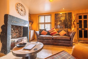 A cozy living room with a fireplace, leather sofa, and a round coffee table. - Spa Cottage - Hot Tub, Cold Pod & Sauna (Morecambe)