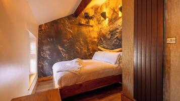 A bedroom with a wooden bed, a nightstand, a wall-mounted light, and a window.