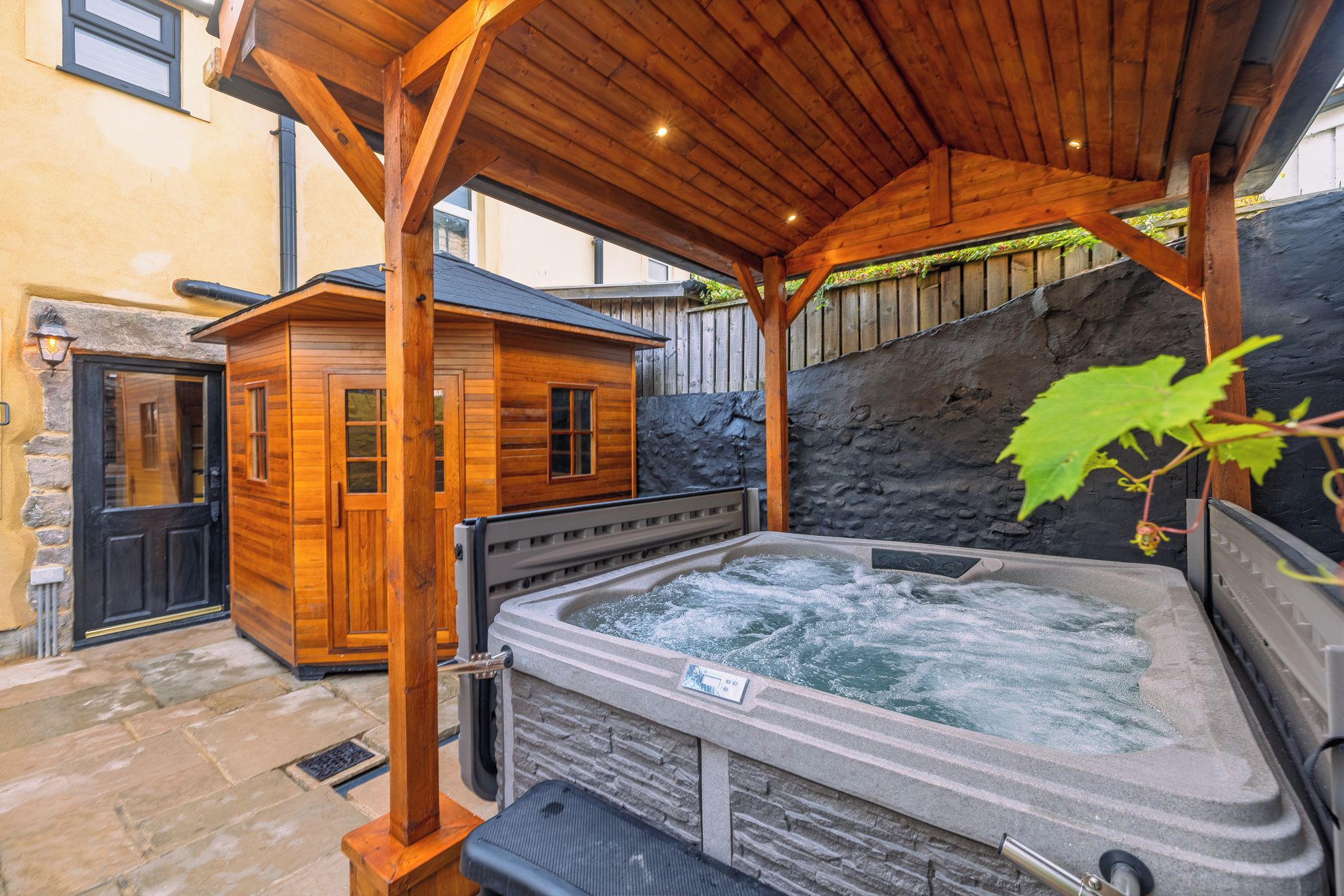 A wooden cabin with a hot tub and a stone wall.