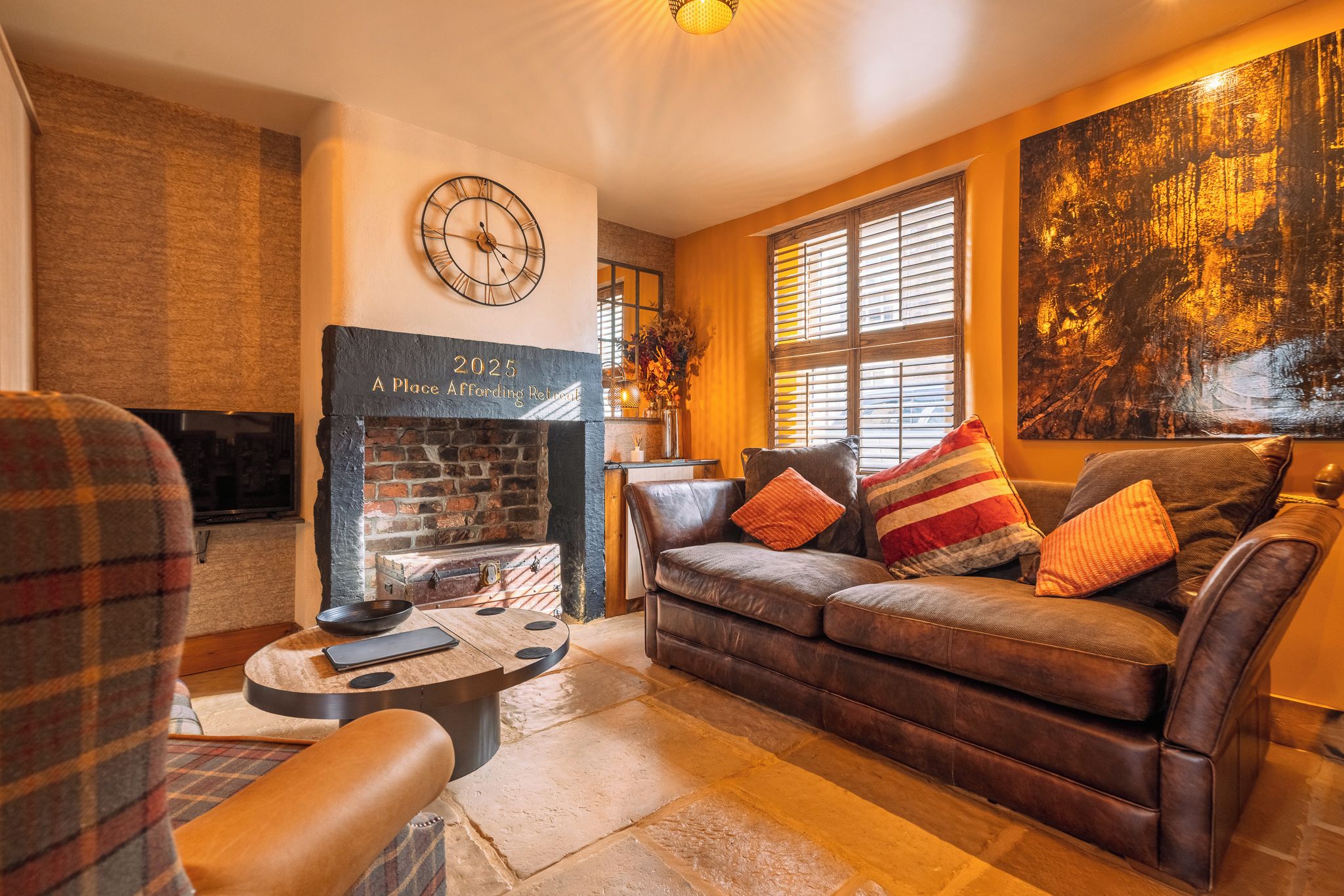 A cozy living room with a fireplace, a sofa with cushions, a coffee table, and a clock on the wall.