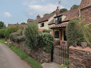 A traditional stone house with a tiled roof, a gated entrance, and lush greenery. - The Cottage (Bridgwater)