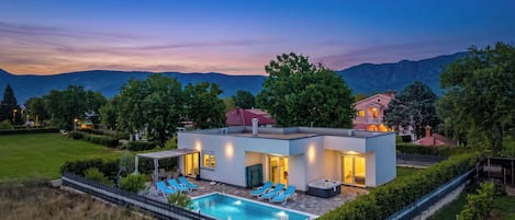 Ein modernes Haus mit Schwimmbad, Sitzgelegenheiten im Freien und Bergblick.