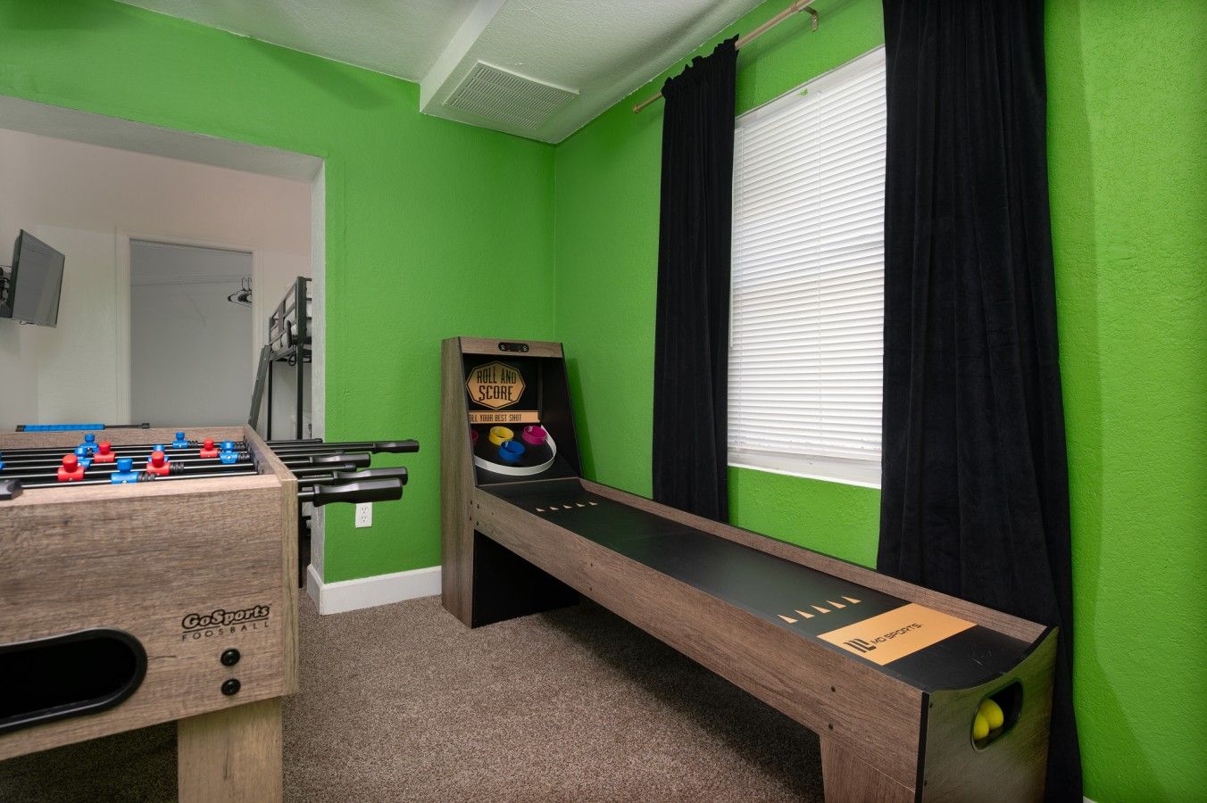 A room with a foosball table, a bowling alley, and a window with curtains.