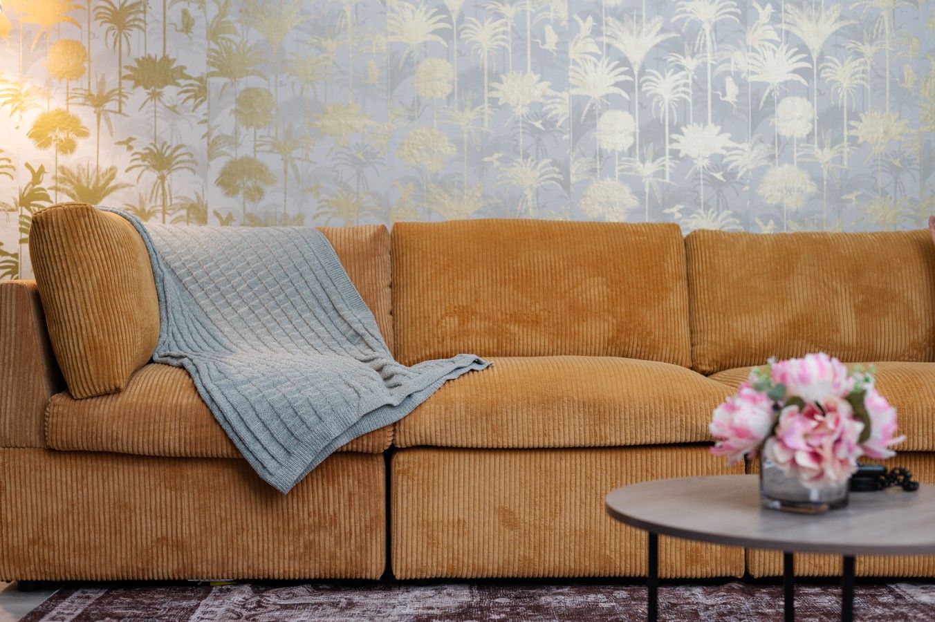 A room with a brown sofa, a blue blanket, and a vase with flowers on a small round table.