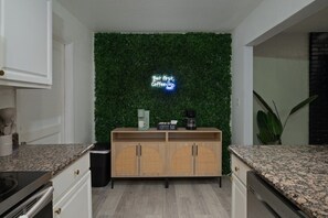A kitchen with a green wall, a coffee bar, and a neon sign.