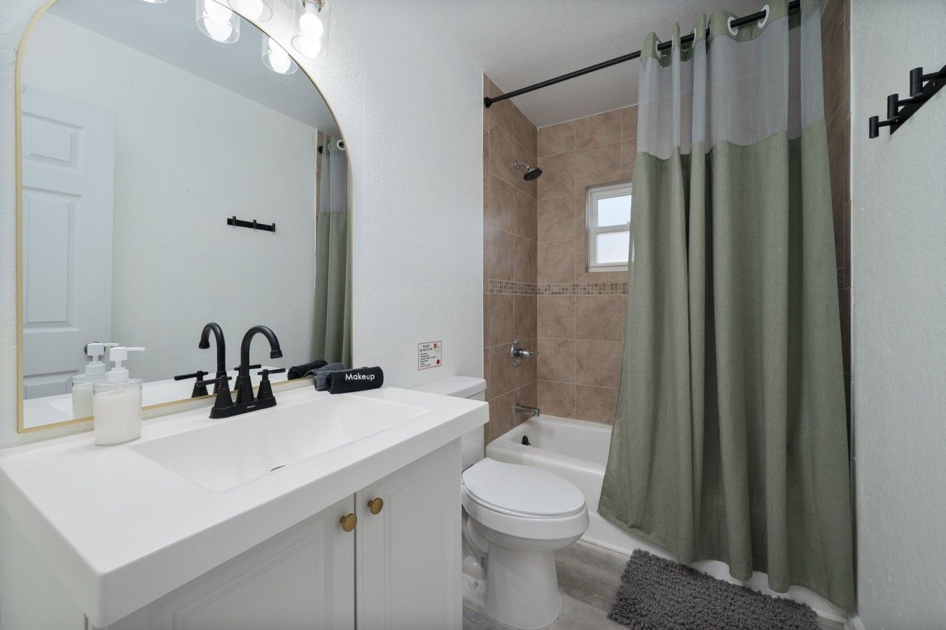 A bathroom with a white sink, black faucet, a mirror, a toilet, and a shower area with a curtain.