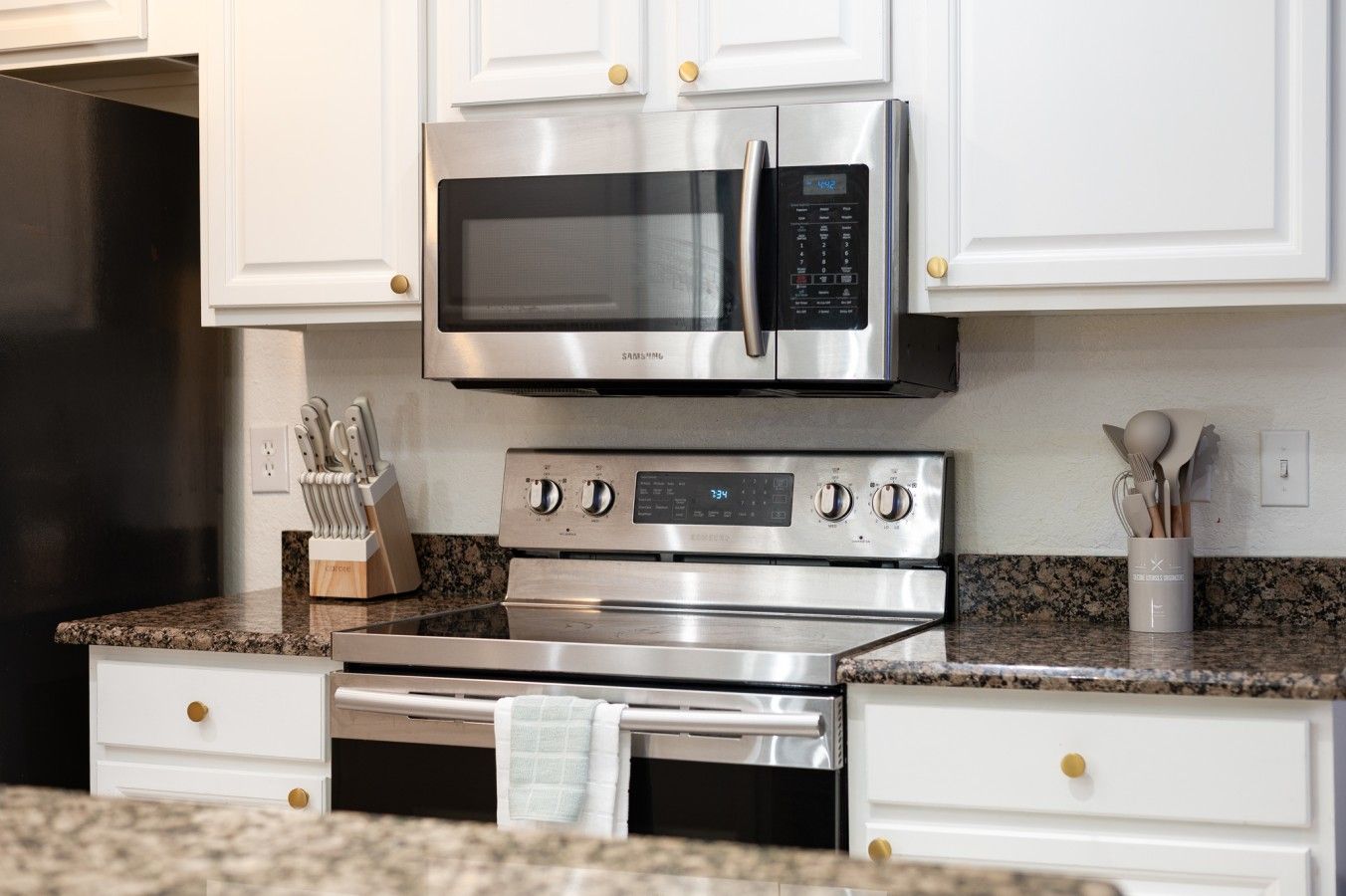 Una cocina con un microondas de acero inoxidable, horno y un juego de cuchillos sobre la encimera.