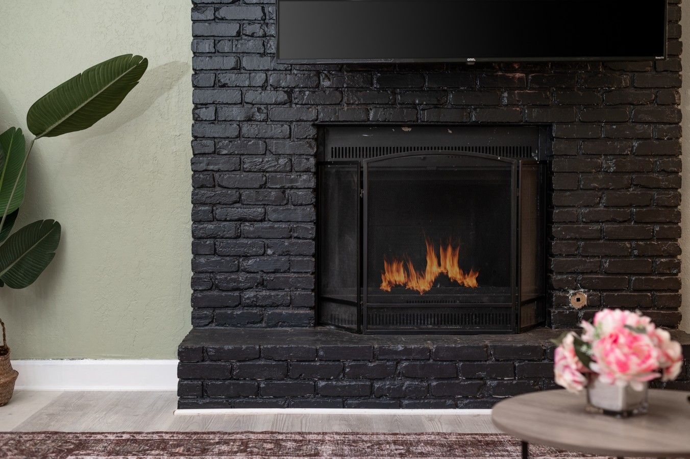 A fireplace with a visible fire, a potted plant, and a vase with flowers.