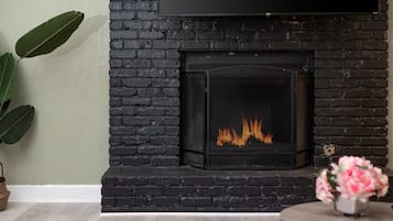 A fireplace with a visible fire, a potted plant, and a vase with flowers.