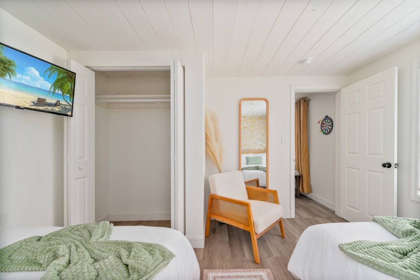 Ein Hotelzimmer mit zwei Betten, einem Kleiderschrank, einem Spiegel und einem an der Wand befestigten Fernseher.