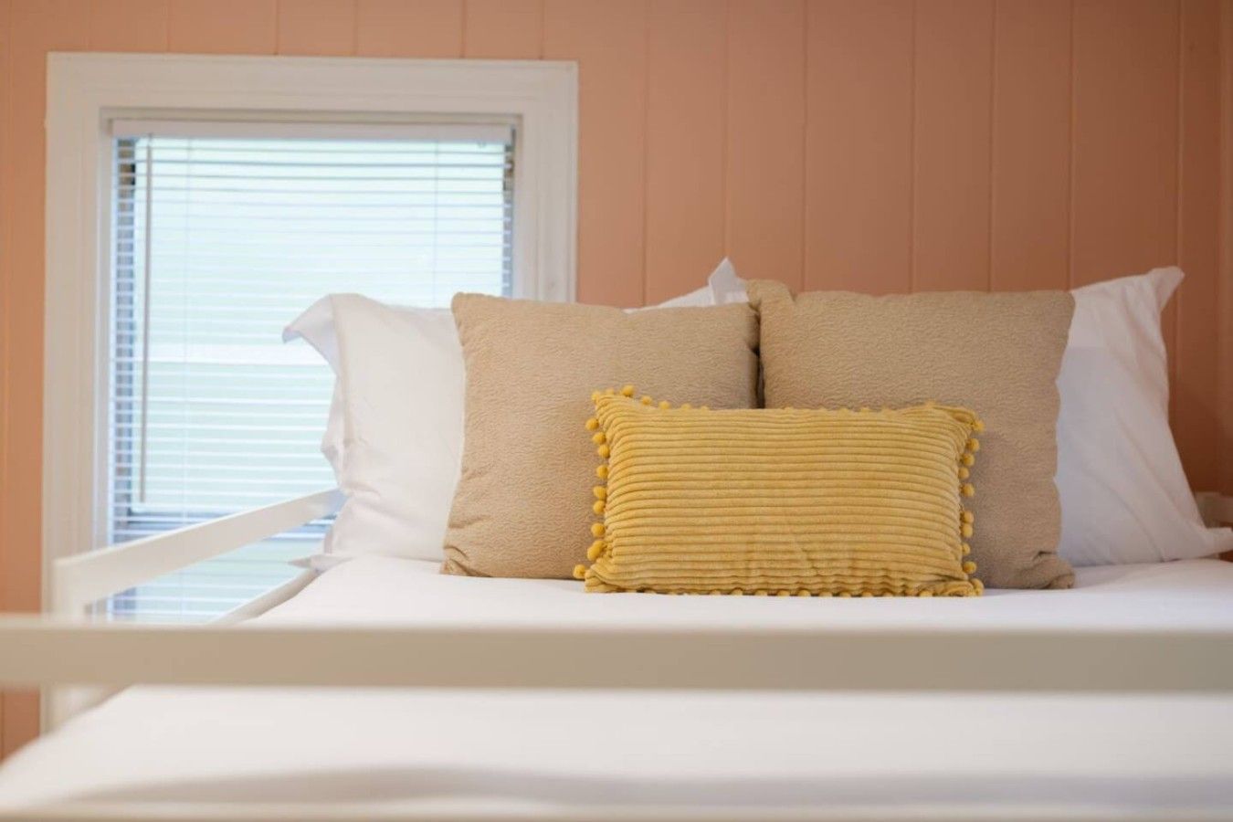 A bed with white bedding and two beige pillows, one with a yellow textured cover.