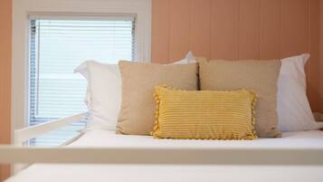 A bed with white bedding and two beige pillows, one with a yellow textured cover.