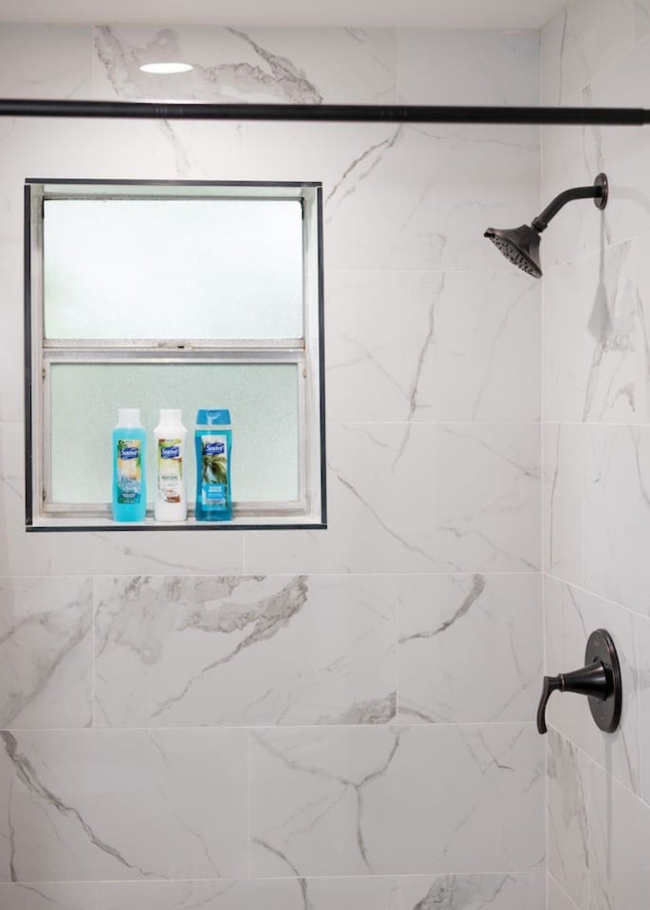 Een badkamer met een douche, een raam en toiletartikelen op de vensterbank.