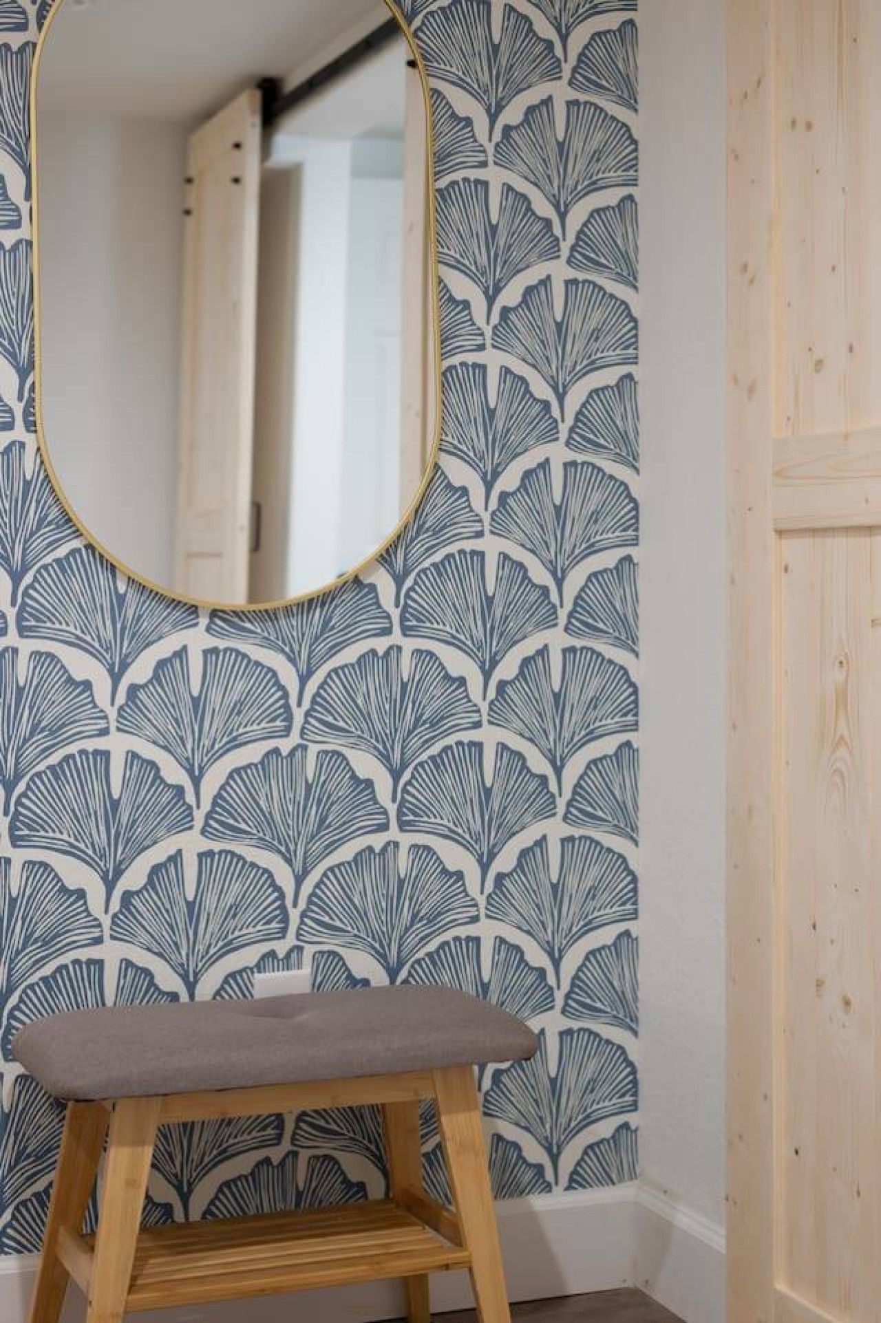 A room with a wooden bench, a mirror on the wall, and a patterned wallpaper.