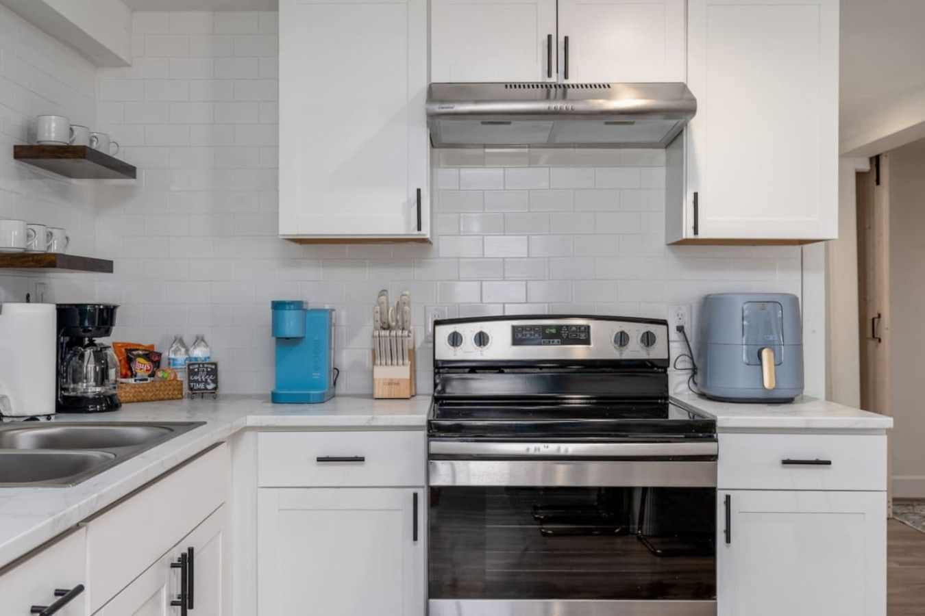 Une cuisine moderne avec des armoires blanches, une hotte de cuisinière en acier inoxydable, une machine à café et une friteuse à air.