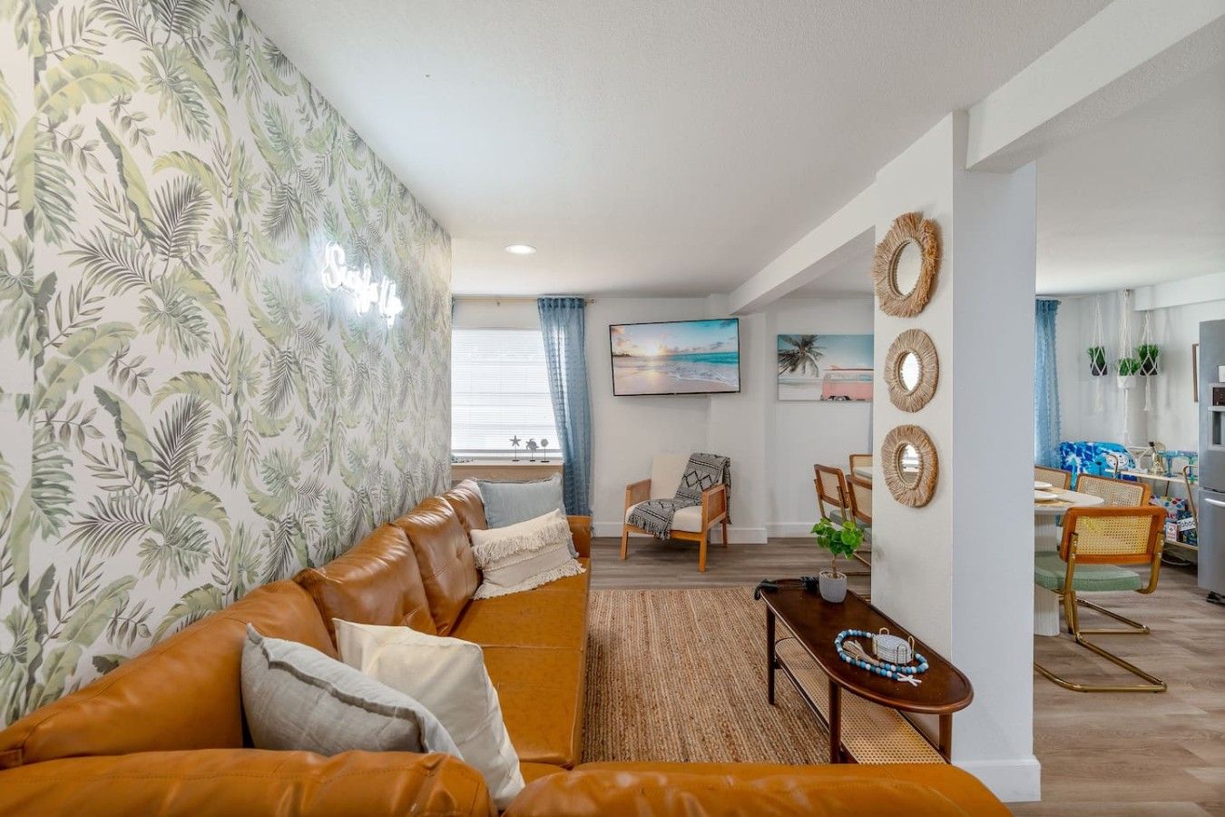 Ein Wohnzimmer mit einer Couch, einem Essbereich mit Stühlen, einem Couchtisch und Blick auf den Strand durch das Fenster.