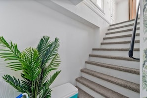 En trappe med gelænder, en potteplante og en hvid væg.