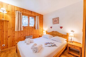 Una habitación con paneles de madera, una cama, dos lámparas de noche, un ventanal con cortinas, un cuadro colgado en la pared y una mesita de noche.