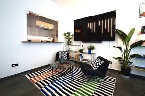 A modern living room with a flat-screen TV mounted on the wall, a glass coffee table, two black armchairs, a striped rug, and a potted plant. - Civita - Designer Apartment - 4 Guests - Near the City Center (Nürnberg)