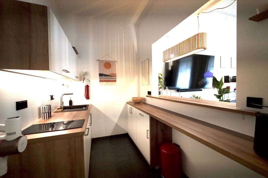 Eine moderne Küche mit einer Holzausziehtheke, einem eingebauten Herd, einer Spüle und einem Fernseher, der über der Theke angebracht ist.
