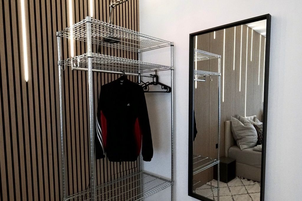 Ein Zimmer mit einem raumhohen Spiegel, einer Kleiderstange und einer gestreiften Wand.