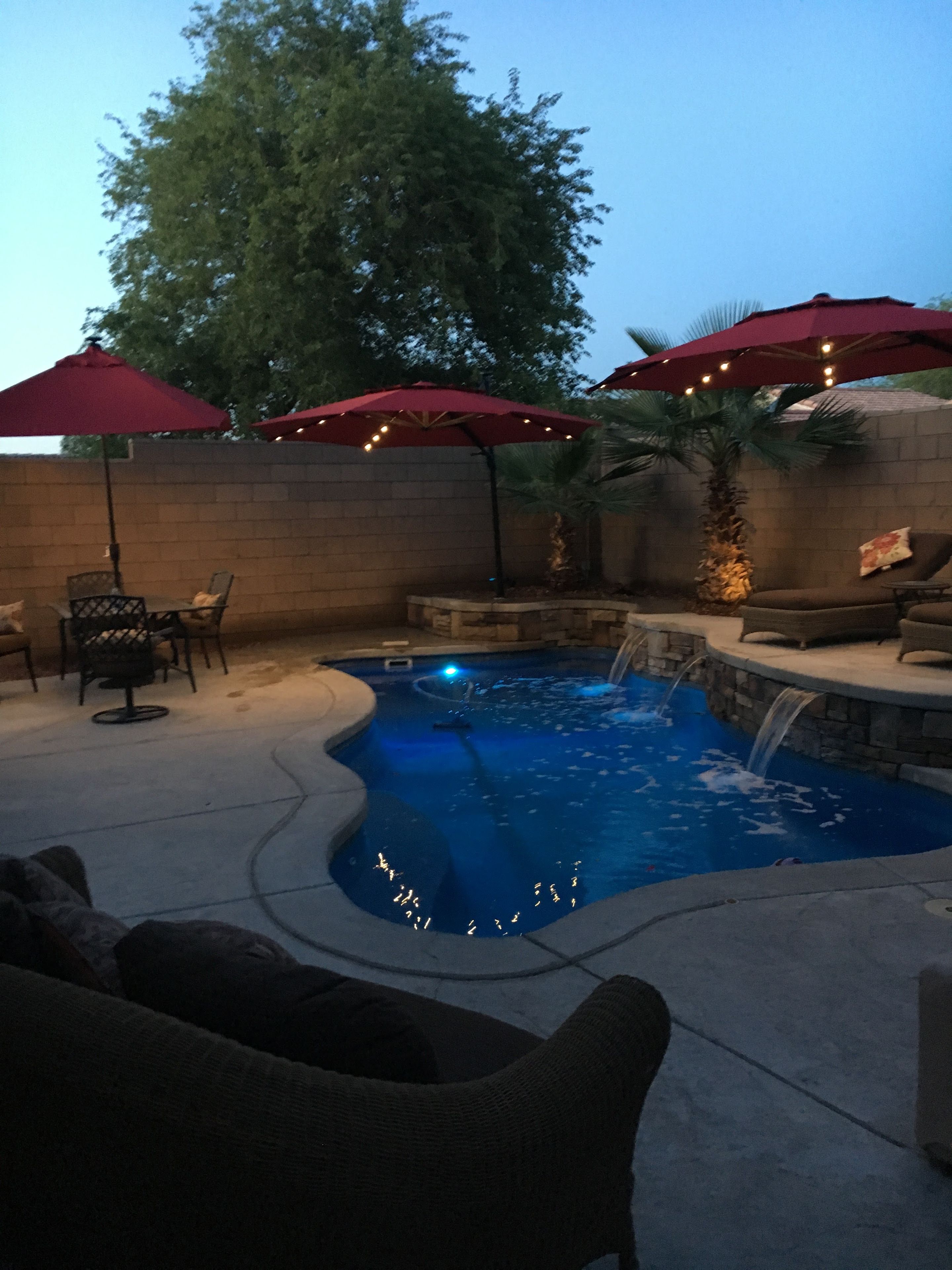 Un jardin avec une piscine, du mobilier d’extérieur et des parasols rouges.
