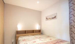 Ein Schlafzimmer mit hölzernem Kopfteil, einem Bett mit gemustertem Überwurf, einem Wandbild und einem Nachttisch mit Lampe.