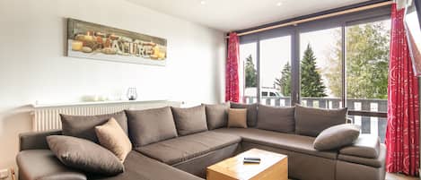 A modern living room with a sectional sofa, a wooden coffee table, and a large window with curtains.